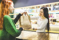 Smiling shop assistant handing over paper bag to customer in a cosmetics shop stock photo
