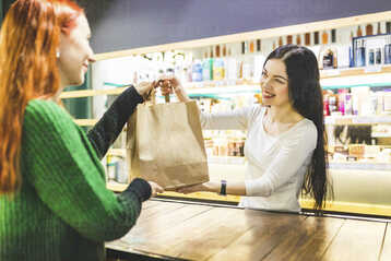 Smiling shop assistant handing over paper bag to customer in a cosmetics shop stock photo